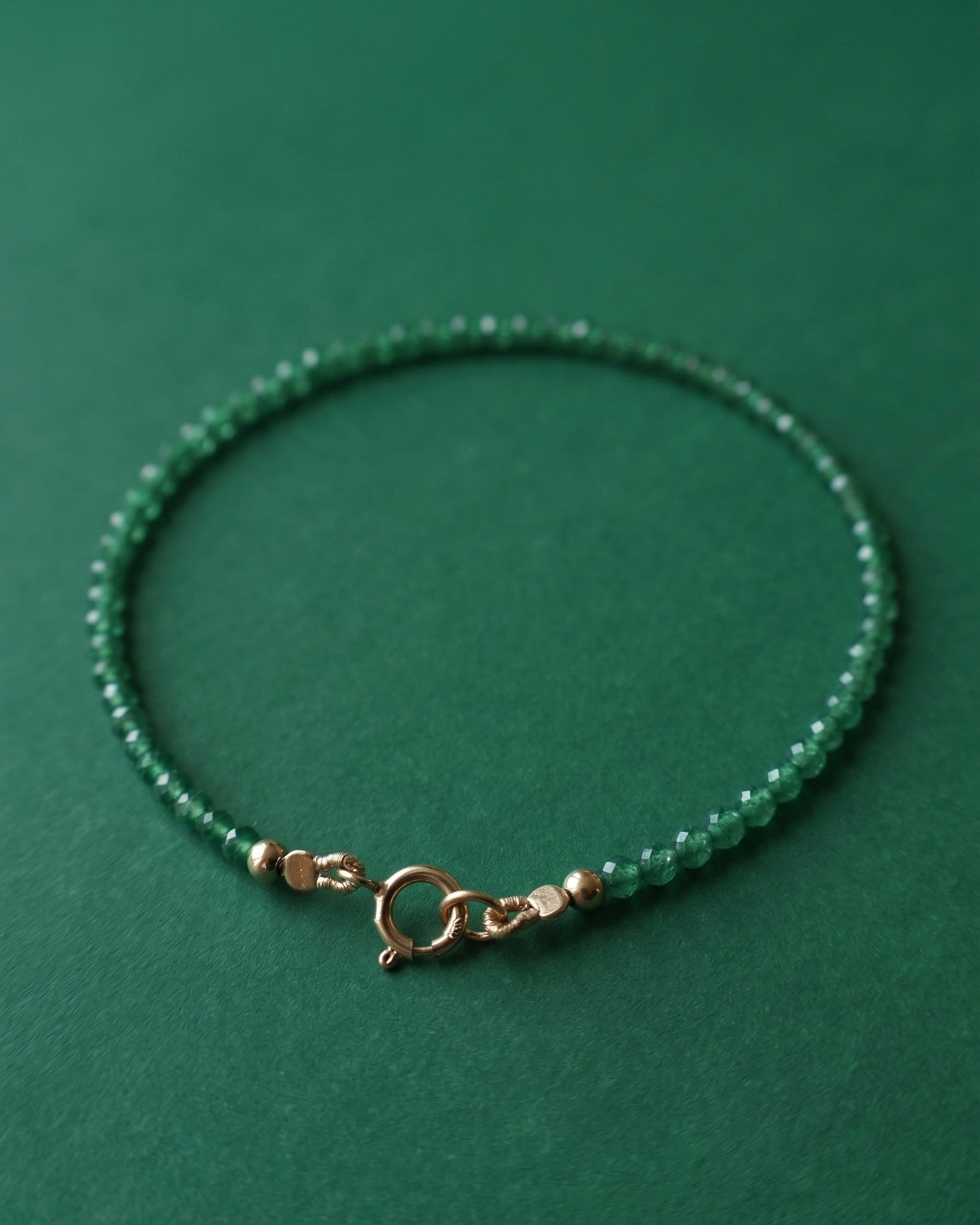 Green beaded bracelet with a gold clasp on a green background